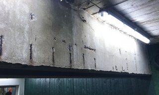 Beschädigte Betonfläche mit freiliegenden Metallstäben unter heller Leuchte